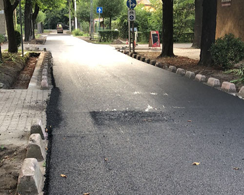 Frissen aszfaltozott utca szegélykővel, fák között